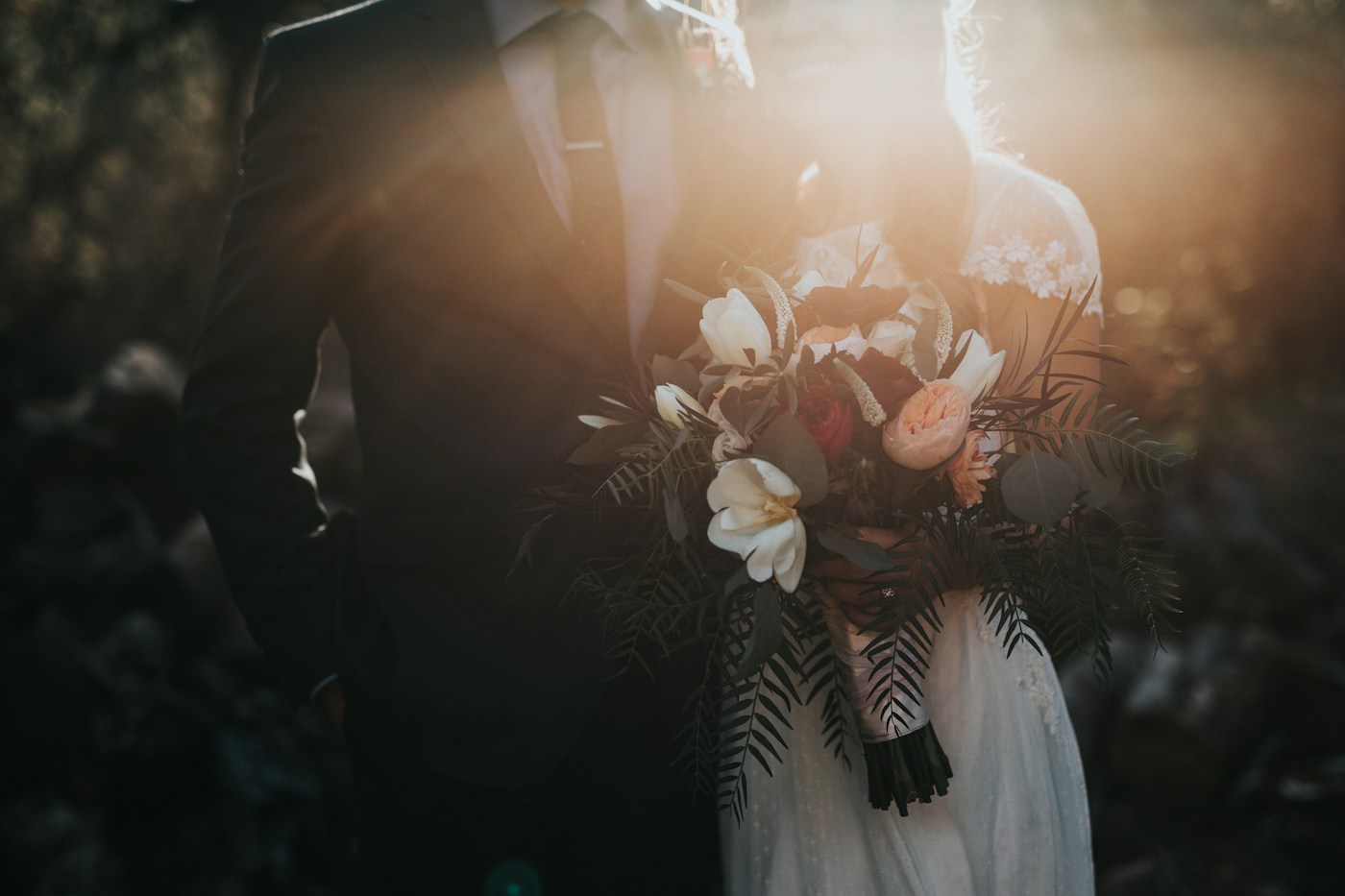 Detalle de una pareja de novios con un ramo de flores, bajo la luz del atardecer